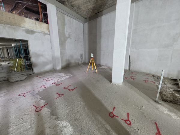 A basement floor slab marked out in red with column and wall positions, a total station set up on a tripod in the background.